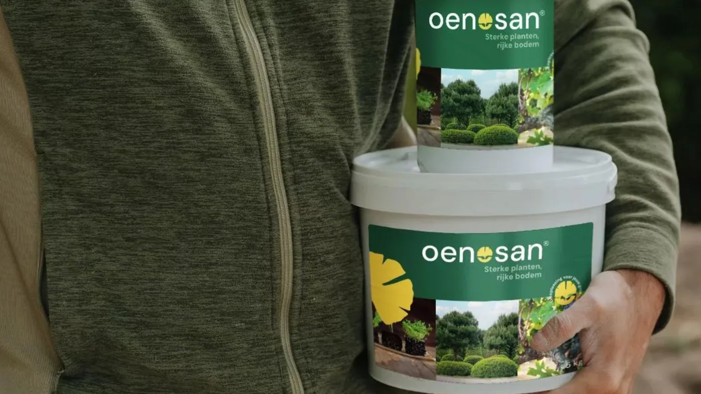 Iemand draagt een emmer en een pot Oenosan over het kwekerijterrein.